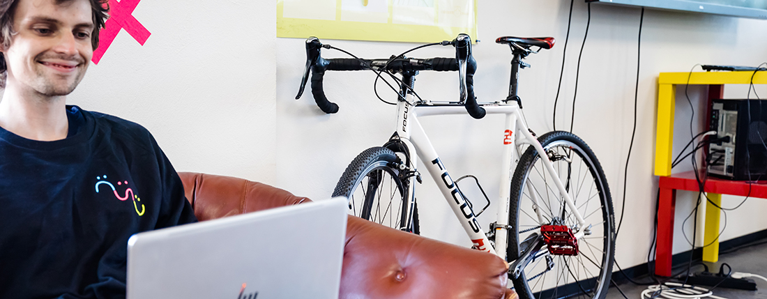 Ein Studierender sitzt vor seinem Laptop, im Hintergrund lehnt ein Rennrad an der Wand