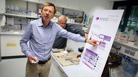 Ein Mann steht in einem Labor vor einem Flipchart und erklärt die Grafik darauf