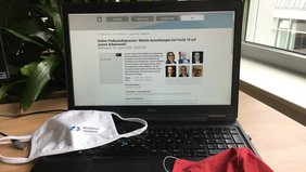 Ein Laptop steht aufgeklappt auf einem Tisch und die Seite Veranstaltungsseite auf der Website der Hochschule Osnabrück wurde aufgerufen. Davor liegen zwei Mund- und Nasenschutzmasken.