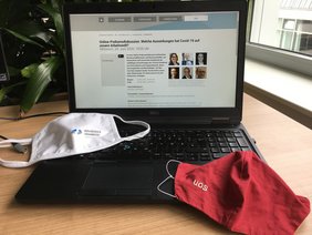 Ein Laptop steht aufgeklappt auf einem Tisch und die Seite Veranstaltungsseite auf der Website der Hochschule Osnabrück wurde aufgerufen. Davor liegen zwei Mund- und Nasenschutzmasken.