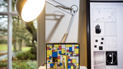 Ein Konstruktion aus bunten Kacheln und einer Holzfigur, die an der Hochschule Osnabrück gebaut wurde, wird von einer Tischlampe beleuchtet und damit in Szene gesetzt.